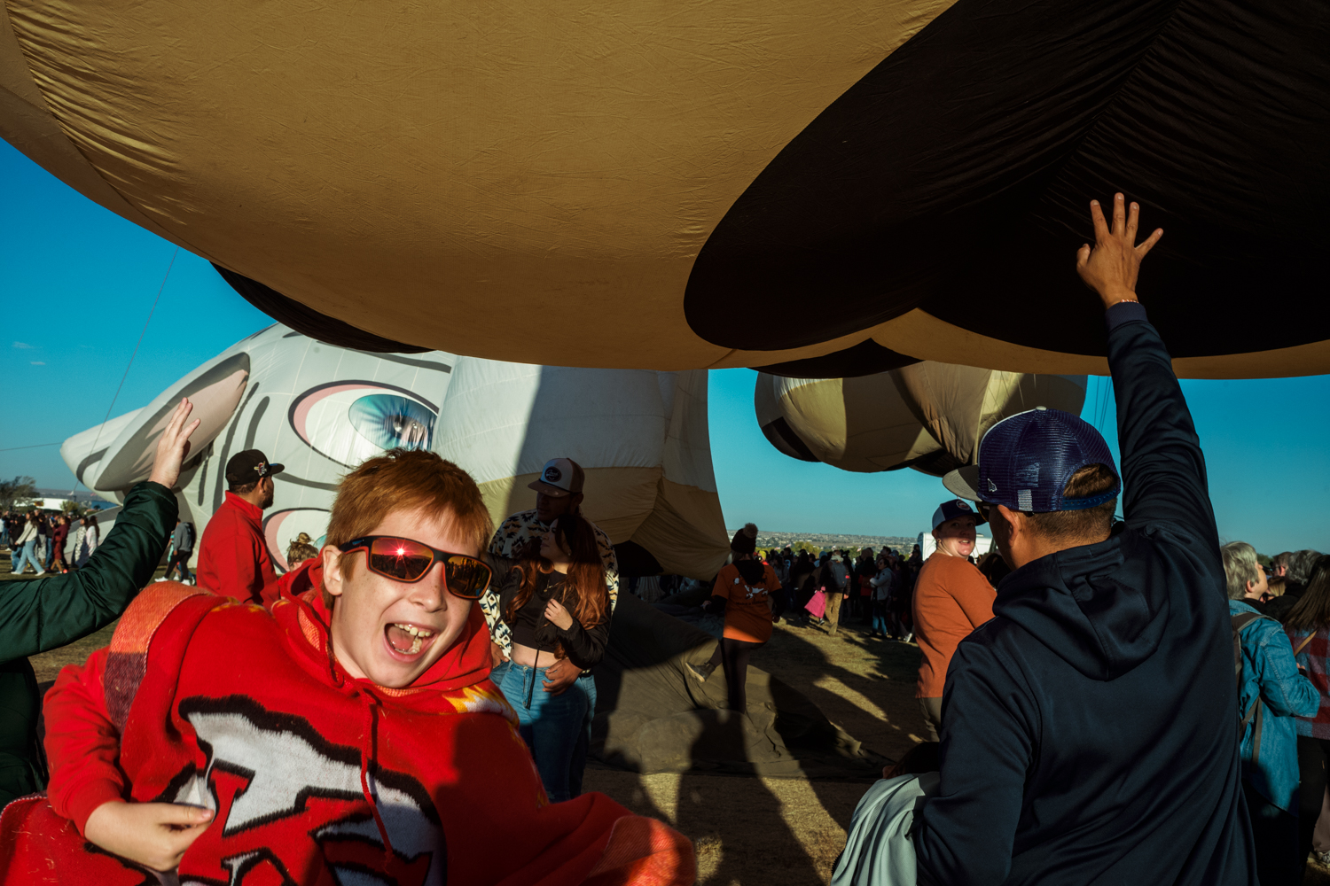 A red-headed boy in sunglasses shouts in glee after touching part of a balloon low overhead