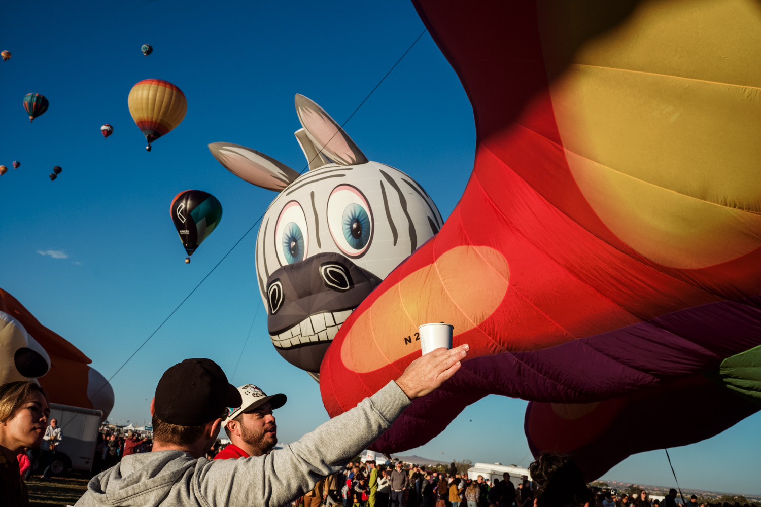 A balloon in the shape of a zebra's head hovers above men pointing towards the distance