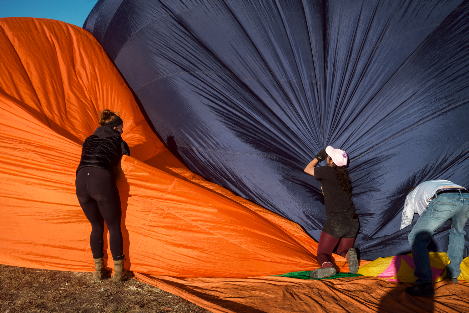 Two women and a man struggle against large segments of billowing orange and dark blue fabric